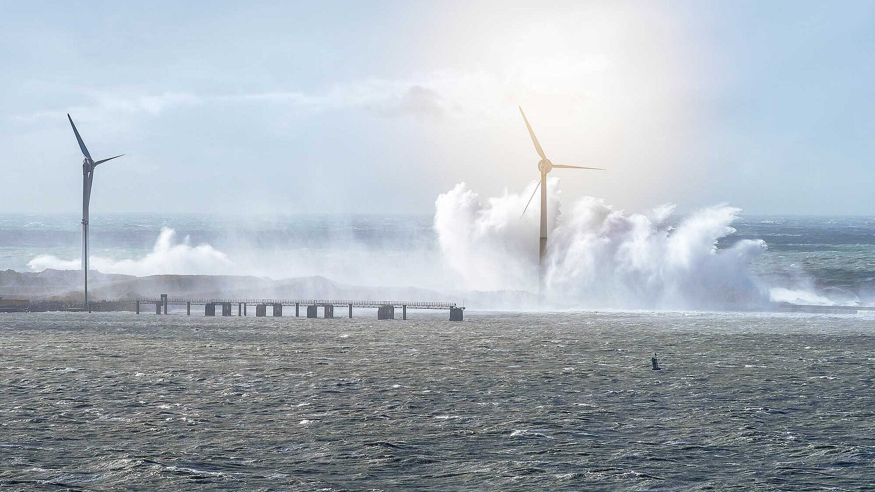 wind turbines in the sea with a blue sky and some waves